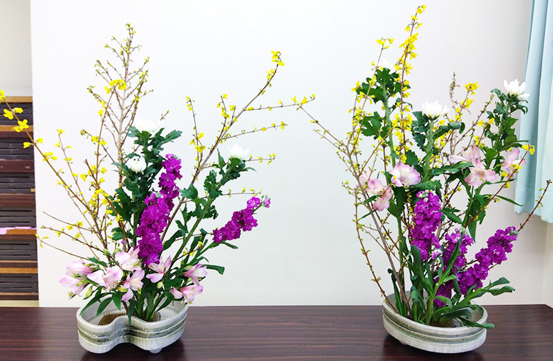 テーブルの上に色鮮やかで伸びやかな生け花が2台のった写真です